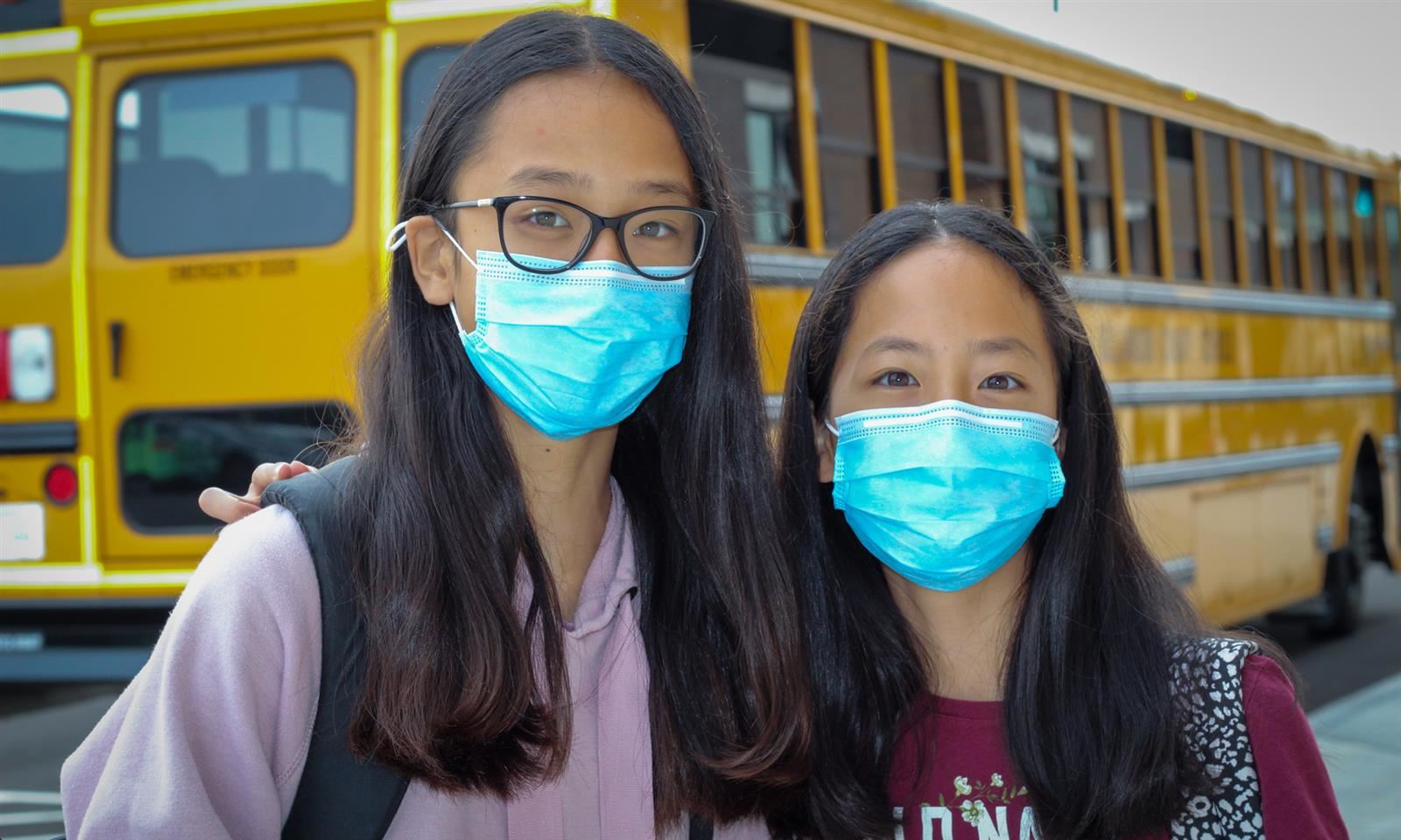 Two girls wearing masks smile